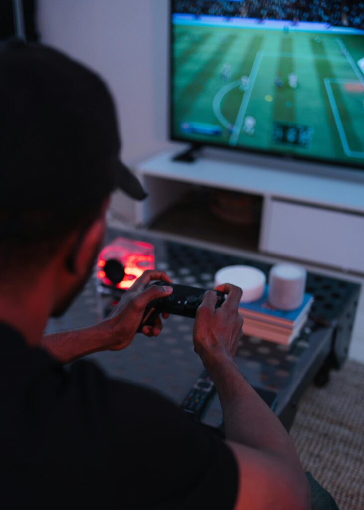 A man playing video games in a modern living room focused on a soccer match on the screen.