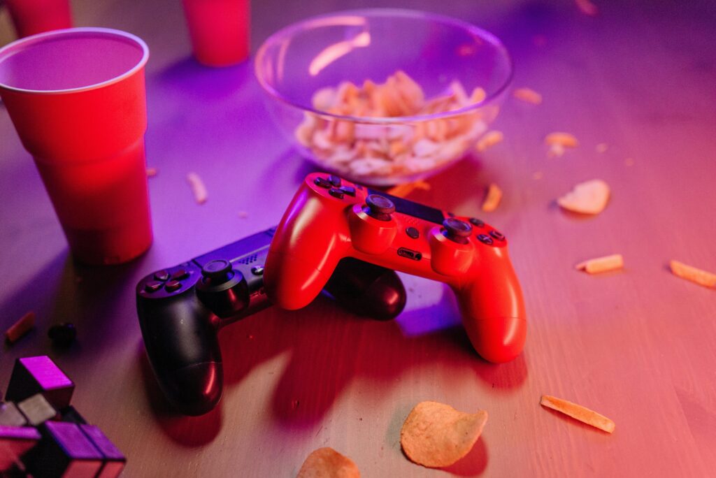 A dynamic gaming setup featuring red and black game controllers, snacks, and vivid lighting.